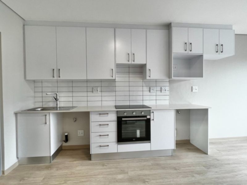 Modern, clean-lined kitchen featuring white cabinetry, subway tile backsplash, integrated electric hob and oven, and light-toned laminate flooring in an open-plan layout.