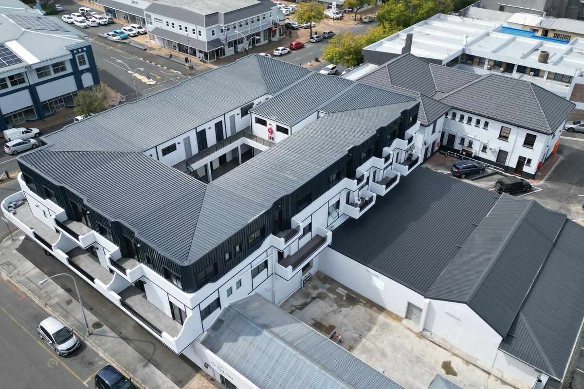 Aerial view of a modern apartment complex featuring a central courtyard, metal roofing, and private balconies with surrounding street-level parking.