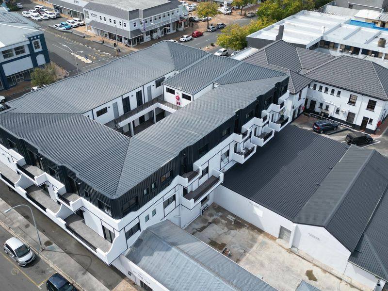 Aerial view of a modern apartment complex featuring a central courtyard, metal roofing, and private balconies with surrounding street-level parking.