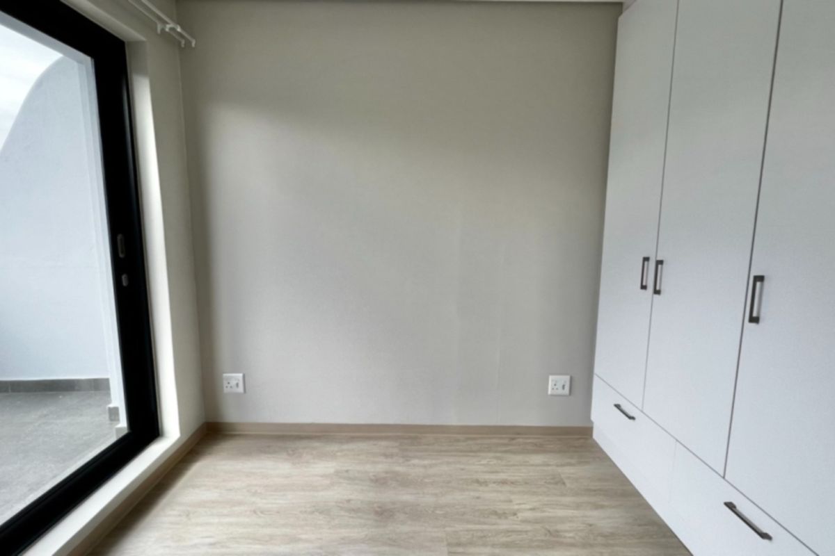A bright, modern bedroom featuring light laminate flooring, built-in cupboards, and a sliding glass door providing access to an outdoor area.