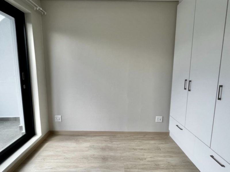 A bright, modern bedroom featuring light laminate flooring, built-in cupboards, and a sliding glass door providing access to an outdoor area.