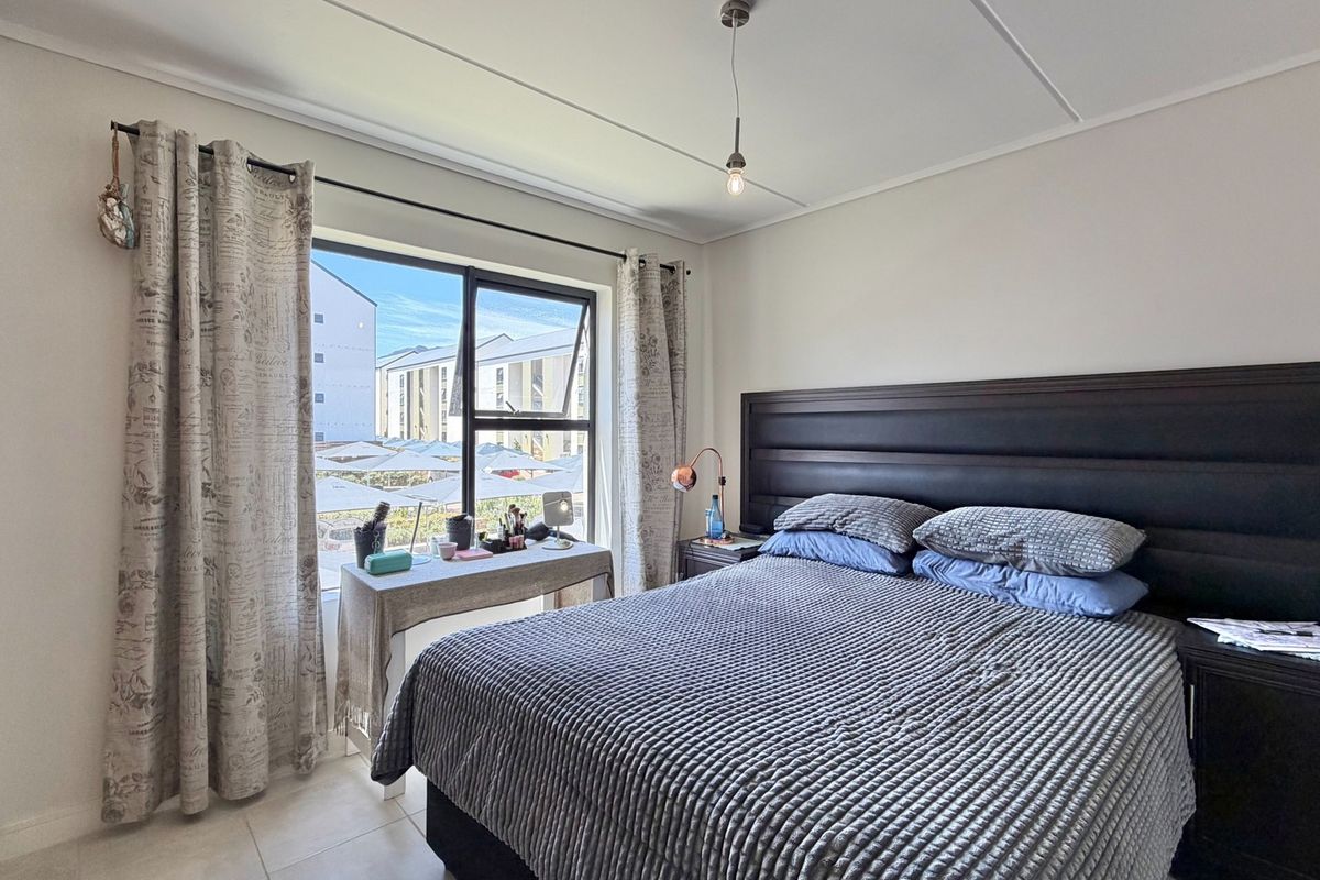 A well-lit bedroom featuring tiled flooring, built-in wardrobe cabinetry, and a large window providing natural light and views of the surrounding complex.