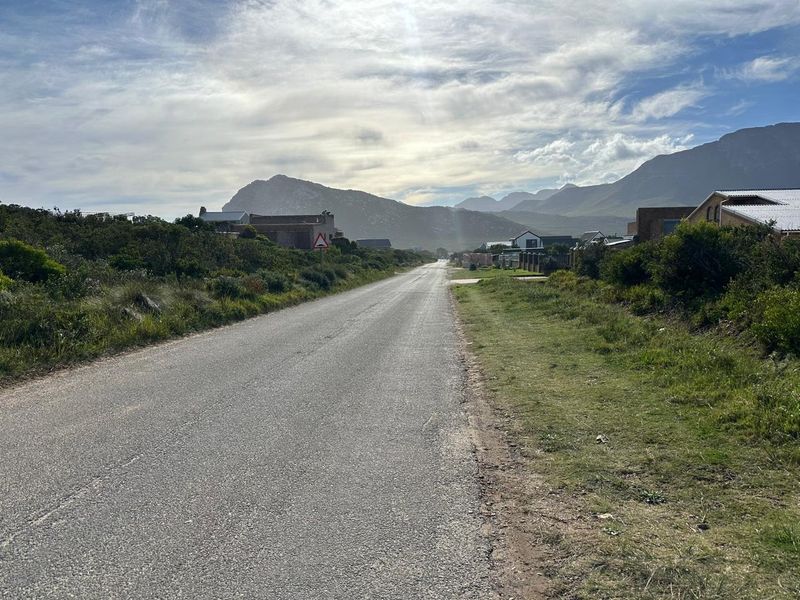 A street view showing the access road leading through a residential area with scenic mountain views in the background.