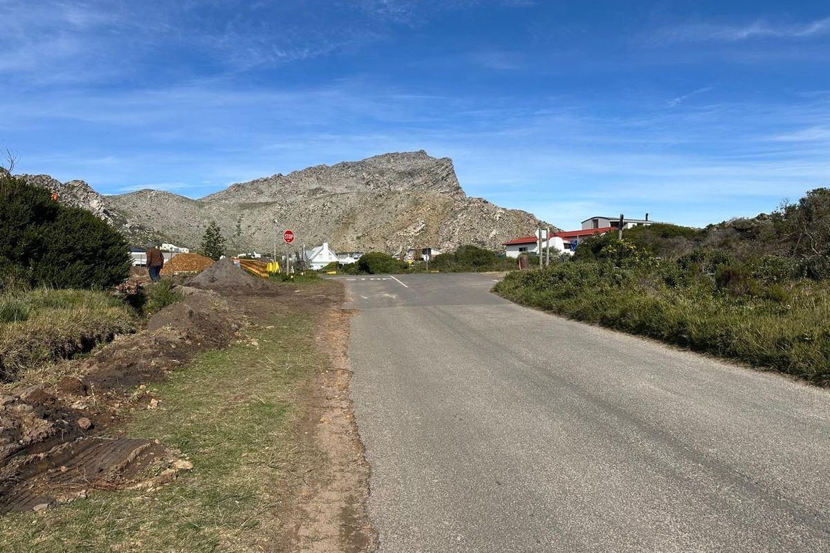 A view of the asphalt street leading towards the residential area with a prominent mountain backdrop.