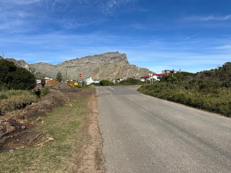 A view of the asphalt street leading towards the residential area with a prominent mountain backdrop.