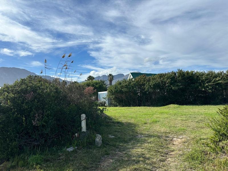 A view of a residential vacant land plot featuring a grass lawn, mature boundary hedges, and scenic mountain views in the background.