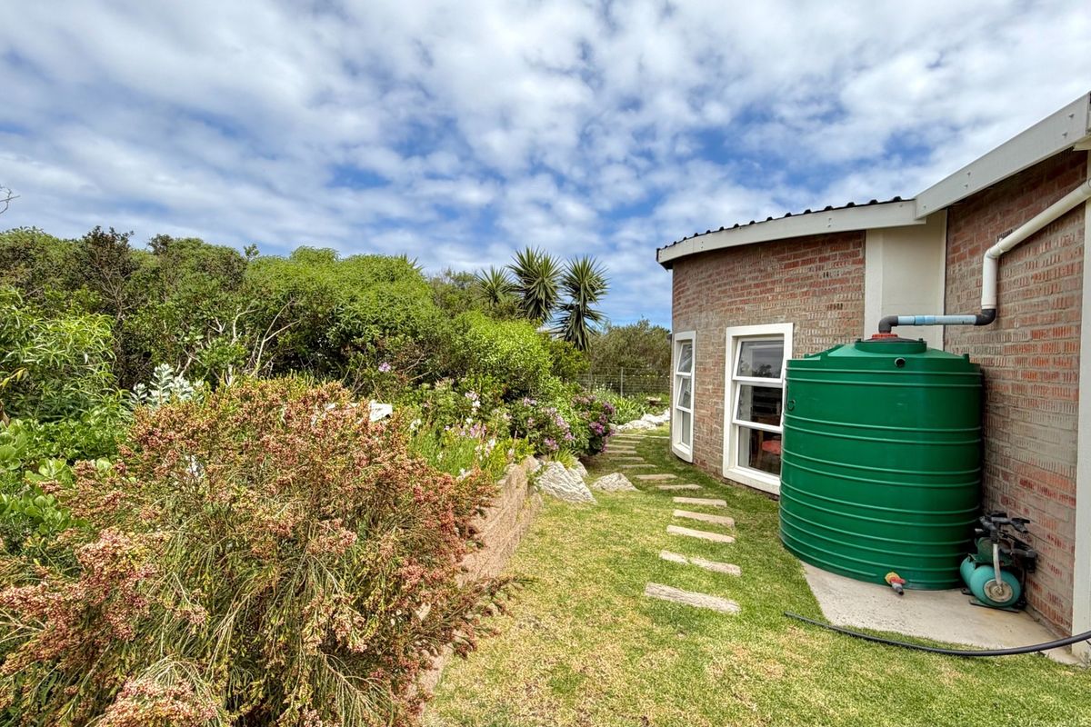 Rear exterior view of the property featuring a brick facade, landscaped garden with a stepped path, and a large green water storage tank.