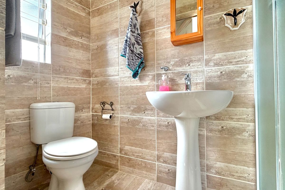 A functional bathroom featuring wood-look wall and floor tiles, a white pedestal sink, a toilet, and a glass-enclosed shower.