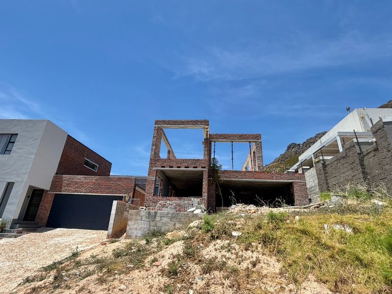 A residential property currently under construction, featuring exposed brickwork, structural concrete elements, and an unfinished facade on a sloped site.
