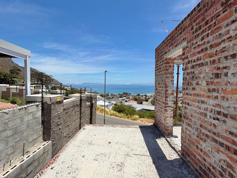 An unfinished construction site featuring exposed brickwork and a concrete slab, offering expansive coastal and mountain views.