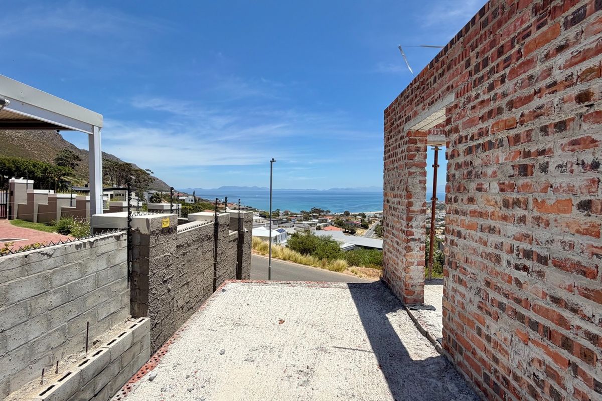 An unfinished construction site featuring exposed brickwork and a concrete slab, offering expansive coastal and mountain views.