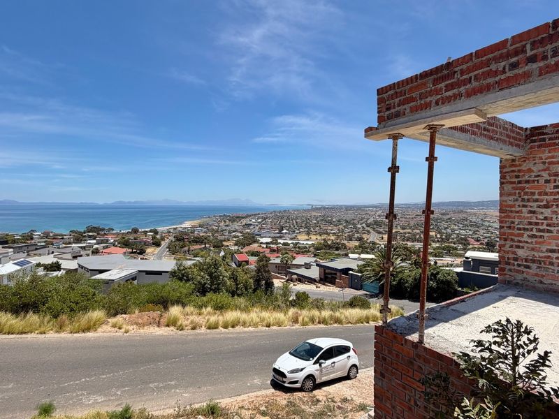 Elevated coastal view from an unfinished construction site featuring exposed brickwork and structural support props.