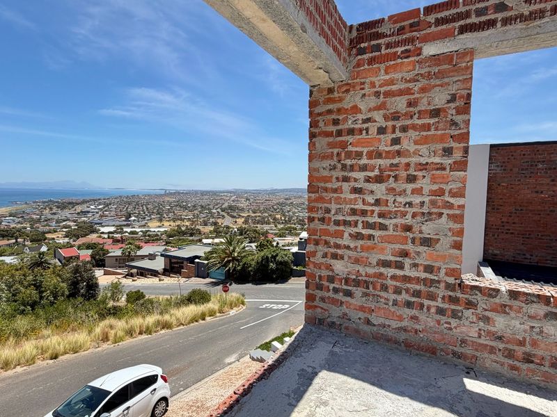 An elevated view from an unfinished construction site featuring exposed brickwork and concrete structural elements overlooking the coastal town and ocean.