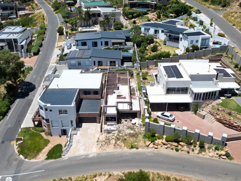 Aerial view of a residential street showing multiple properties, including a home currently under construction with exposed brickwork.