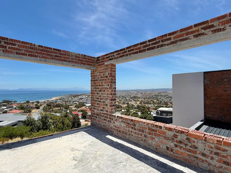 An unfinished construction site showing exposed brickwork and concrete structure with panoramic coastal and urban views.