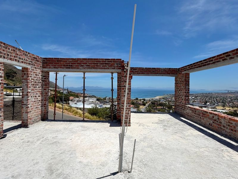 An unfinished construction site featuring exposed brick walls and concrete flooring with panoramic coastal and urban views.