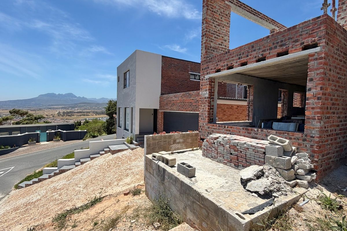 A property under construction featuring exposed brickwork and concrete structural elements, situated on a sloped lot with views of the surrounding area.