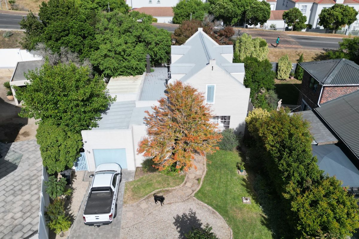 Aerial view of the property showcasing the main building, metal roofing, paved driveway, garage, and established garden area.