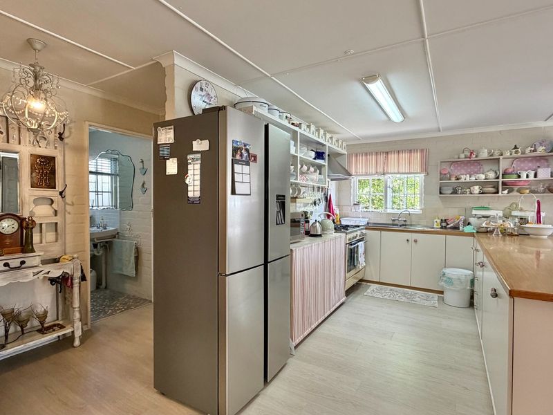 A functional kitchen featuring built-in cabinetry, open shelving, a gas stove with extractor fan, and a breakfast counter, with an adjacent utility area.