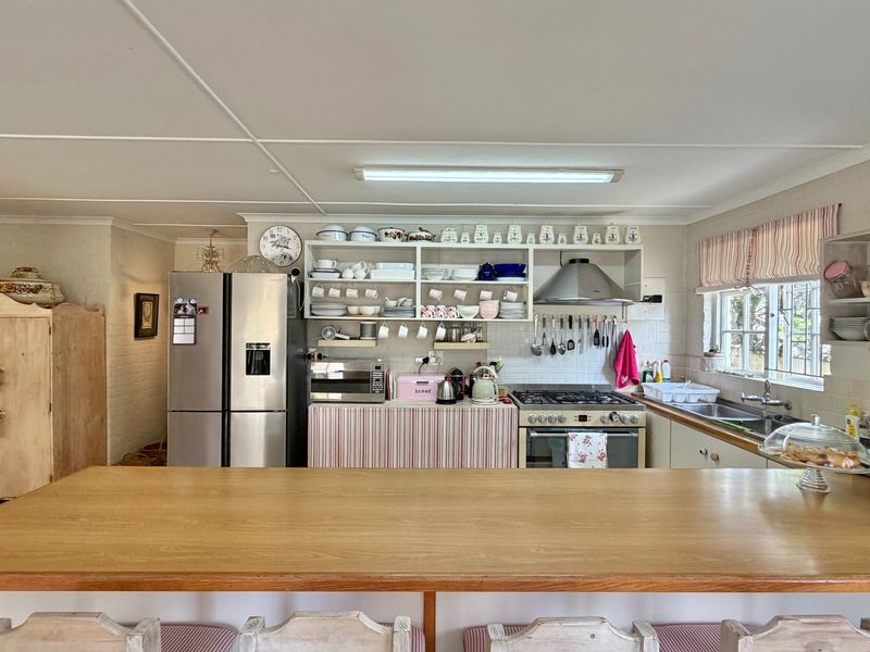 A functional kitchen featuring a gas hob, extractor fan, stainless steel sink, and a wooden breakfast bar with ample open shelving.