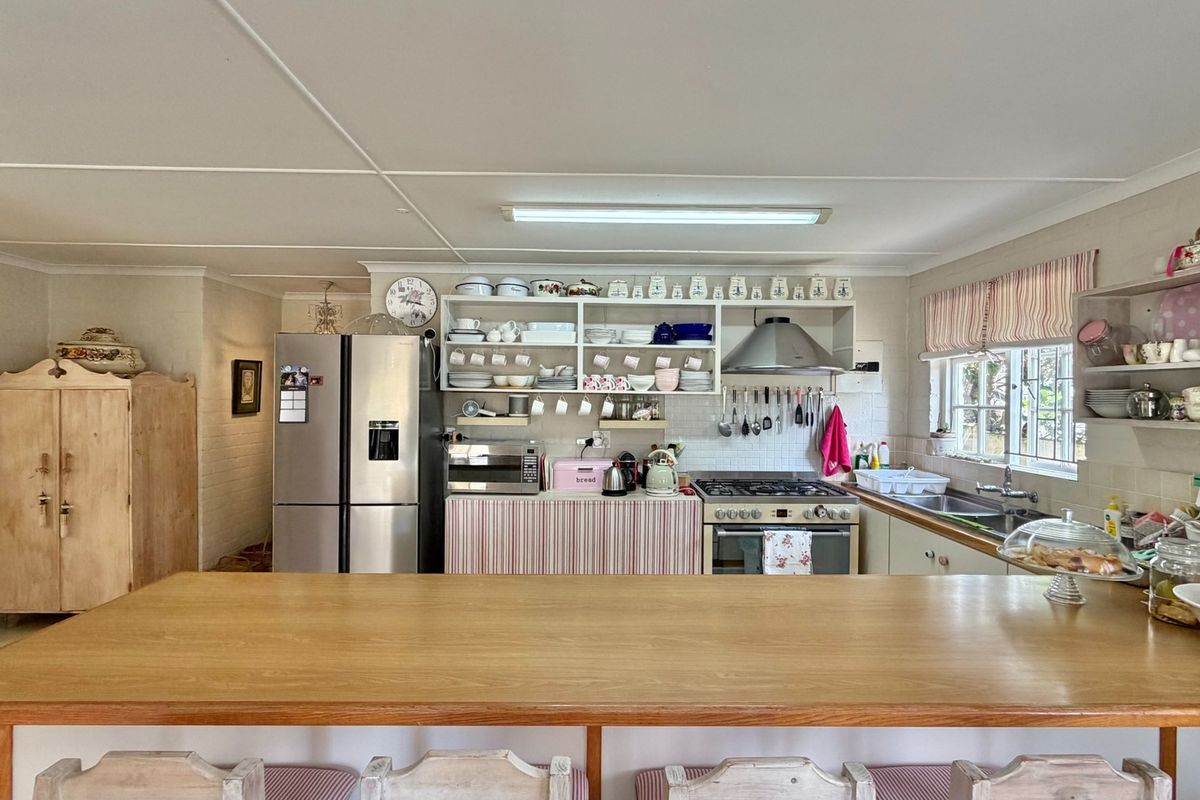 A functional kitchen featuring a gas hob, extractor fan, stainless steel sink, and a wooden breakfast bar with ample open shelving.