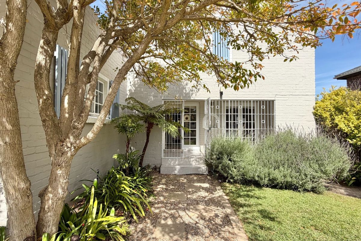 A well-maintained rear exterior view featuring a painted brick facade, secure gated entrance, and a landscaped garden with a stone pathway.