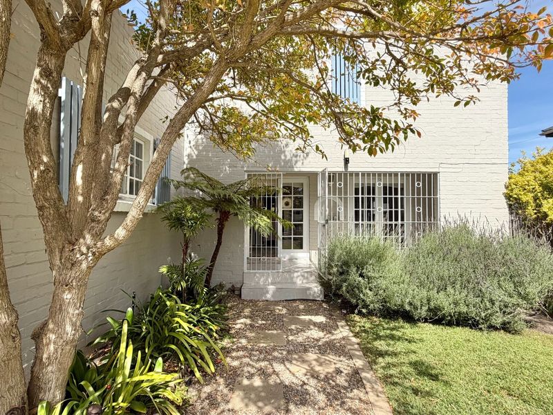 A well-maintained rear exterior view featuring a painted brick facade, secure gated entrance, and a landscaped garden with a stone pathway.