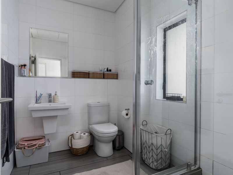 A functional bathroom featuring a wall-mounted basin, toilet, and a glass-enclosed shower with tiled finishes throughout.