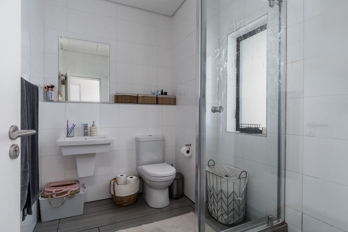 A functional bathroom featuring a wall-mounted basin, toilet, and a glass-enclosed shower with tiled finishes throughout.