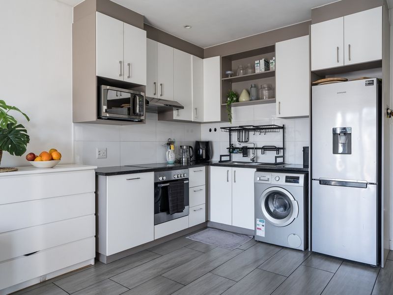 A modern, compact kitchen featuring white cabinetry, stone countertops, integrated appliances, and tiled flooring, offering a clean and functional cooking space.