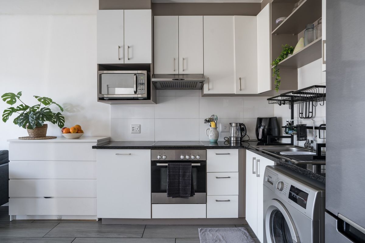 A modern, compact kitchen featuring white cabinetry, dark countertops, integrated appliances, and a tiled backsplash, offering efficient storage and workspace.