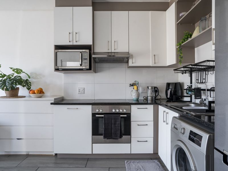 A modern, compact kitchen featuring white cabinetry, dark countertops, integrated appliances, and a tiled backsplash, offering efficient storage and workspace.