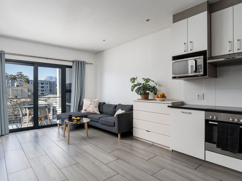 Modern open-plan apartment living area featuring a sleek kitchen with built-in appliances and large sliding doors leading to a balcony with urban views.