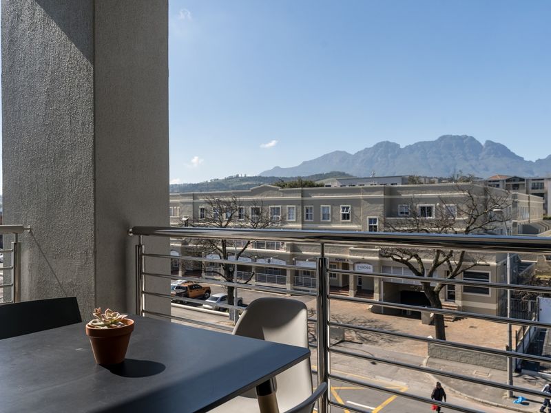 A private balcony featuring a stainless steel balustrade and offering clear views of the surrounding neighborhood and mountain range.