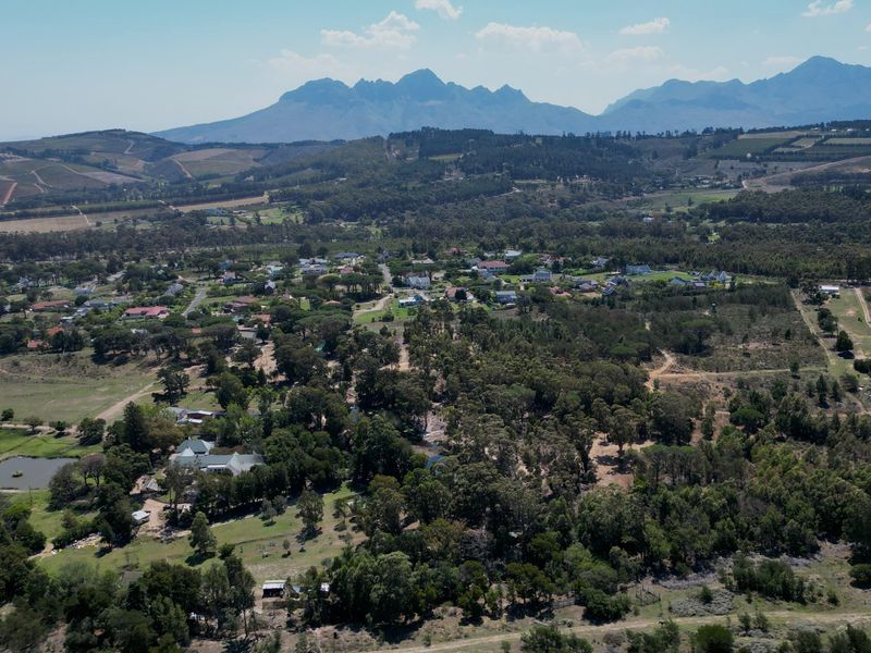 An expansive aerial view of a rural residential area surrounded by lush greenery and scenic mountain ranges in the distance.
