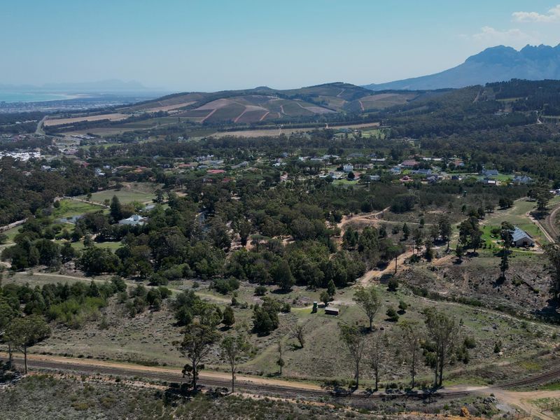 An aerial view of a large vacant residential land plot featuring natural vegetation, an adjacent railway line, and surrounding rural landscape.