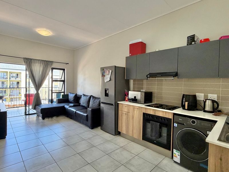 Open-plan living area featuring a modern kitchen with built-in cabinetry, integrated appliances, and tiled flooring, leading to a private balcony.