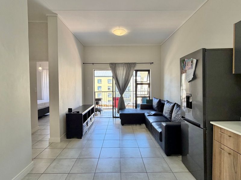 Open-plan living area featuring tiled floors, a compact kitchen space, and direct access to a private balcony.