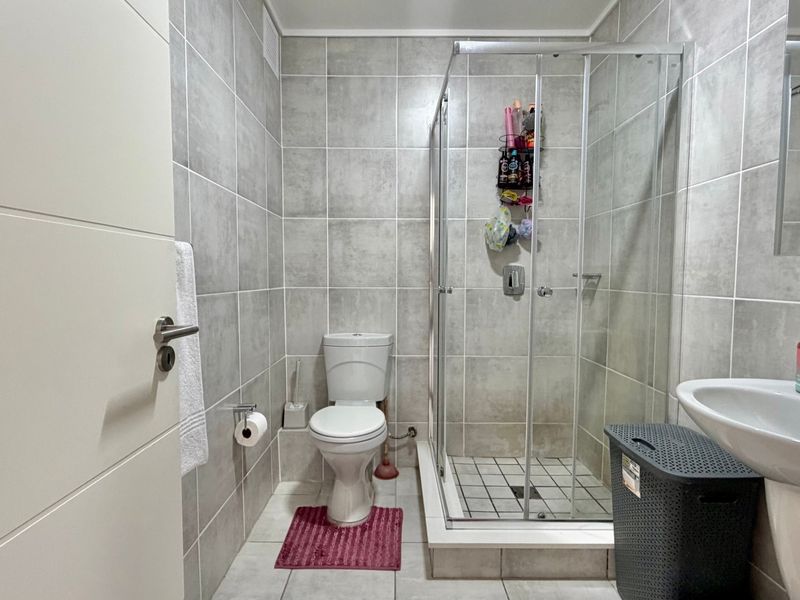 A modern bathroom featuring grey tiled walls and flooring, a glass shower enclosure, a pedestal basin, and a standard toilet.