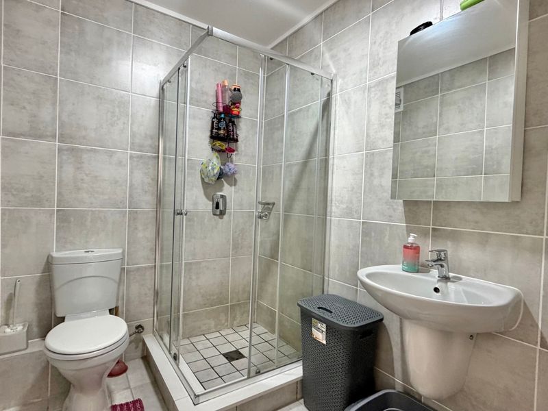 A functional bathroom featuring a glass shower enclosure, pedestal basin, toilet, and neutral wall tiling throughout.