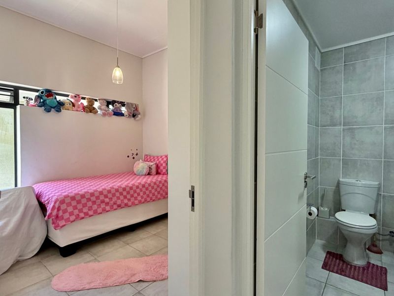 A bedroom featuring tiled flooring and pendant lighting, with an adjacent bathroom equipped with a shower and toilet.