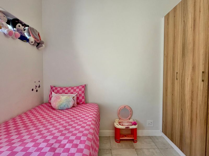 A compact bedroom featuring light-toned wood-finish built-in wardrobes, tiled flooring, and a high-level window providing natural light.