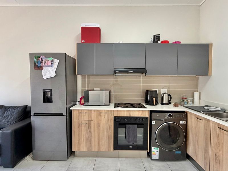 Compact open-plan kitchen featuring modern wood-finish cabinetry, integrated oven and hob, tiled backsplash, and a functional stainless steel sink area.