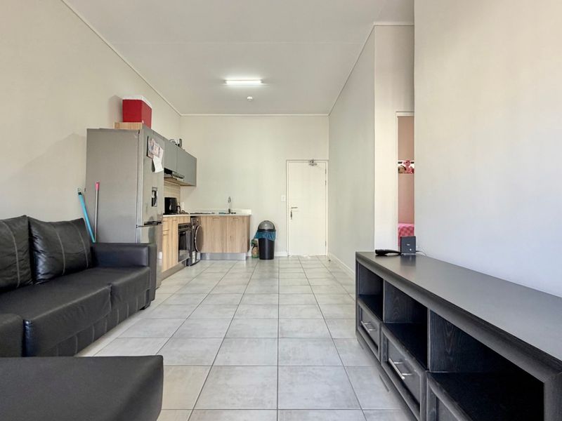 Open-plan living area featuring a compact kitchen with built-in cabinetry, oven, and hob, finished with neutral tiled flooring throughout.
