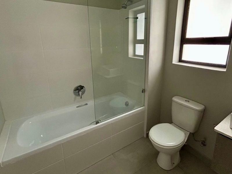 A clean, modern bathroom featuring a bathtub with a glass shower screen, a toilet, and a vanity with a vessel sink.