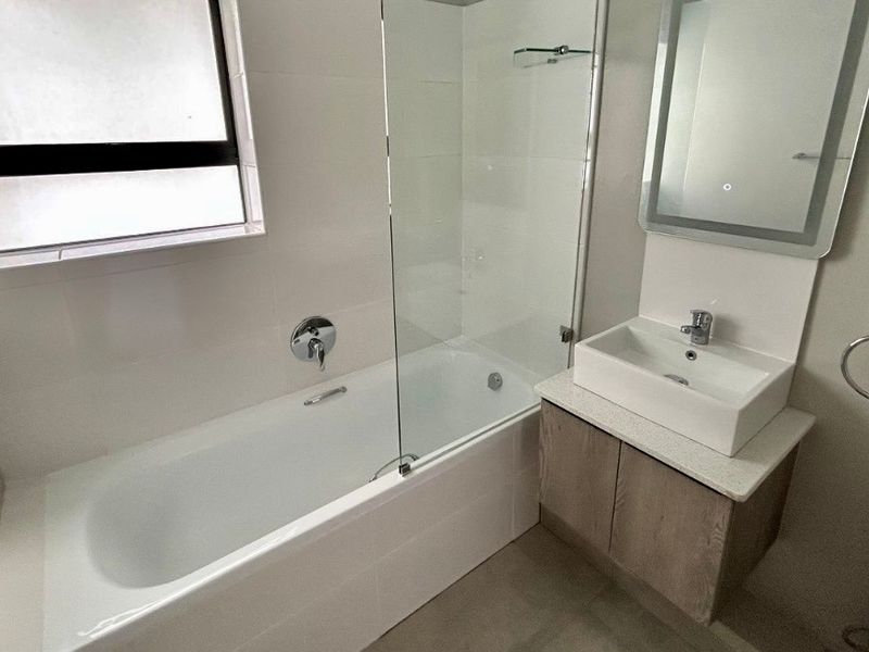 Modern bathroom featuring a bathtub with a glass screen, a contemporary vanity with a vessel sink, and a sleek wall-mounted mirror.