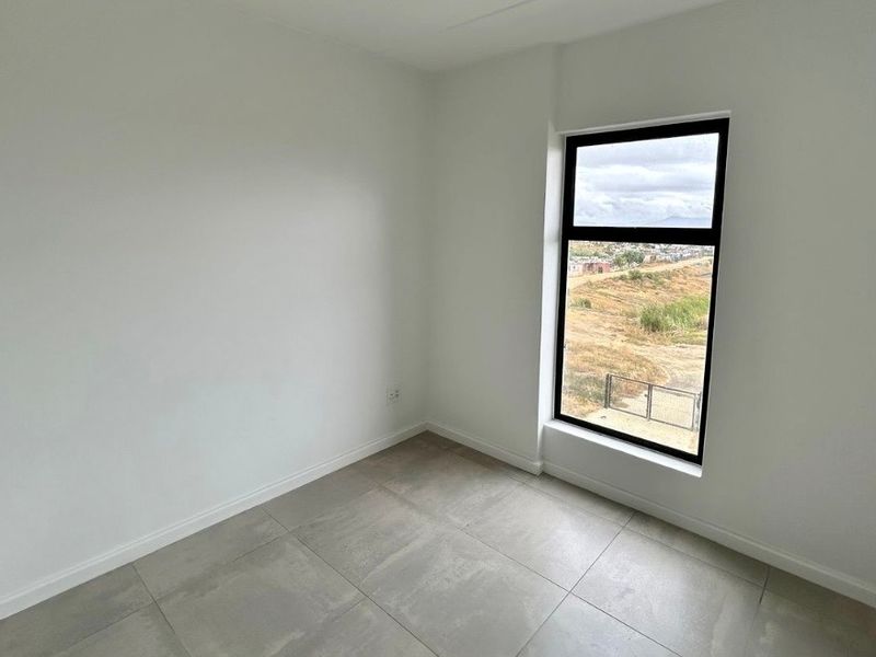A bright, empty bedroom featuring modern tiled flooring, a built-in cupboard, and a large window with views of the surrounding landscape.