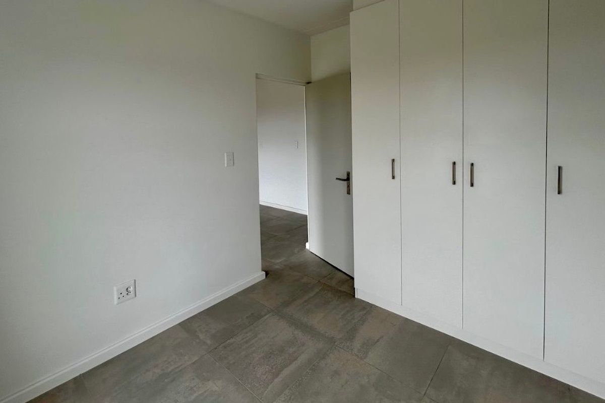 A clean, empty bedroom featuring neutral tiled flooring and ample built-in cupboard storage, offering a blank canvas for personalization.