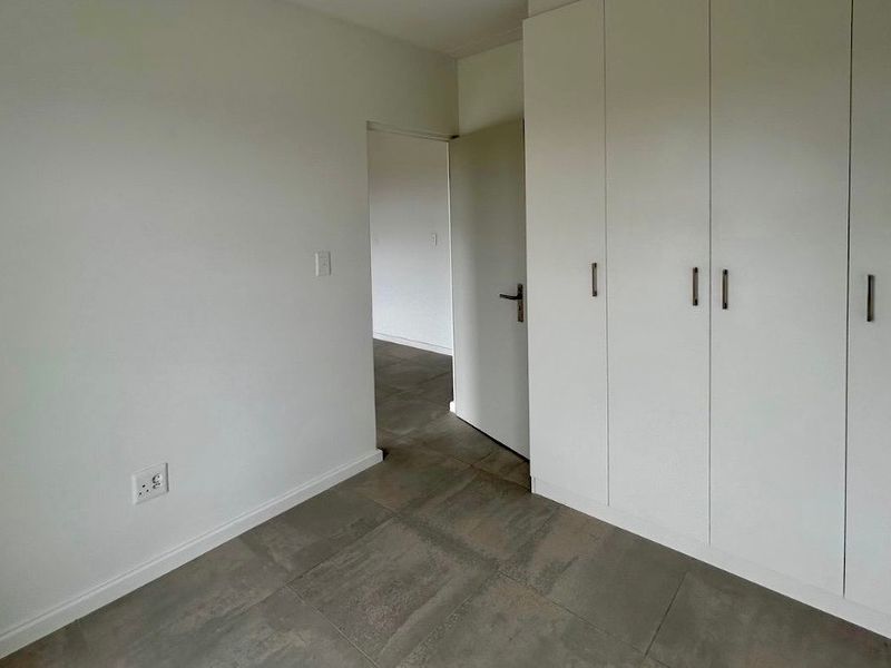A clean, empty bedroom featuring neutral tiled flooring and ample built-in cupboard storage, offering a blank canvas for personalization.
