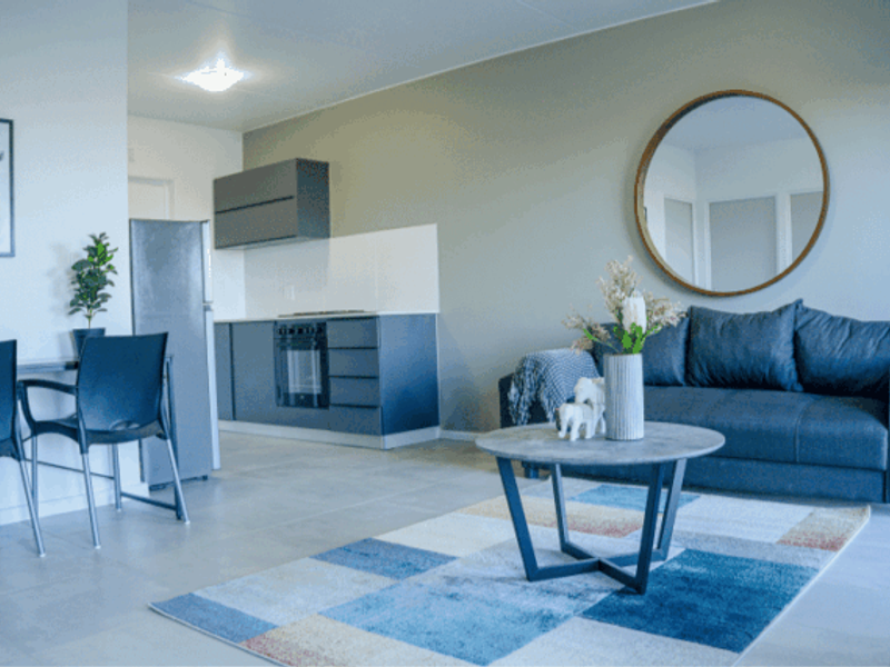 Modern open-plan living area featuring a sleek kitchen with built-in cabinetry, integrated oven, and tiled flooring, seamlessly flowing into the lounge space.